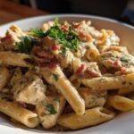 A close-up of creamy Chicken Bacon Ranch Penne pasta, garnished with parsley and bacon bits.
