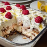 A slice of Chocolade Lasagne dessert in a glass dish, topped with whipped cream, raspberries, and lemon zest.