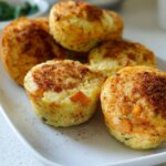 A close-up of several Cinnamon Apple Cottage Cheese Bites on a white plate, sprinkled with cinnamon.