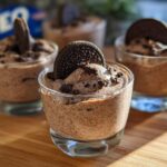 Close-up of individual glasses filled with creamy Cookies and Cream Mousse, topped with crushed cookies and an Oreo.