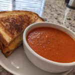 A bowl of creamy tomato basil soup next to a golden-brown grilled cheese sandwich, perfect for soup recipes.