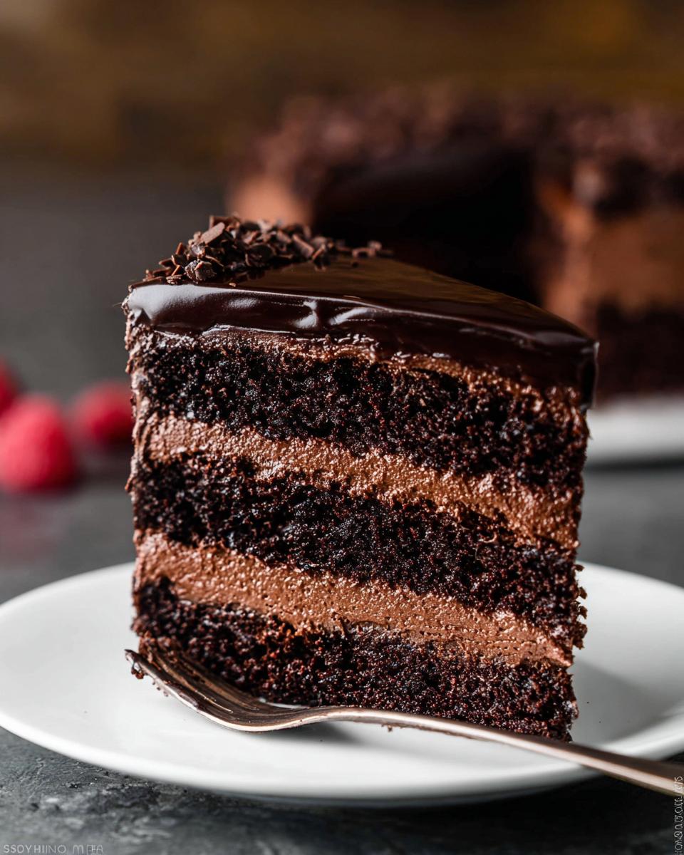 A decadent slice of Dark Chocolate Mousse Cake with layers of chocolate cake and mousse, topped with chocolate glaze and shavings.