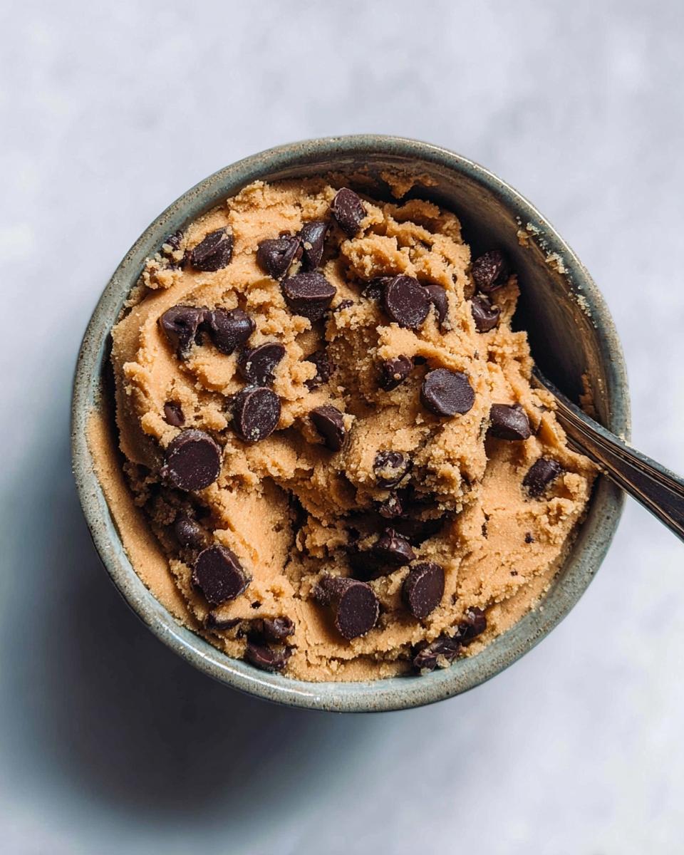 A close-up overhead view of a bowl filled with Delicious Protein Cookie Dough studded with chocolate chips.