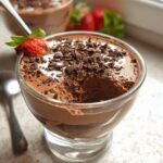 A close-up of a glass bowl filled with Easy Cottage Cheese Chocolate Mousse, topped with chocolate shavings and a strawberry.