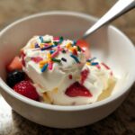A bowl of easy frozen Greek yogurt topped with fresh strawberries, blueberries, and colorful sprinkles.