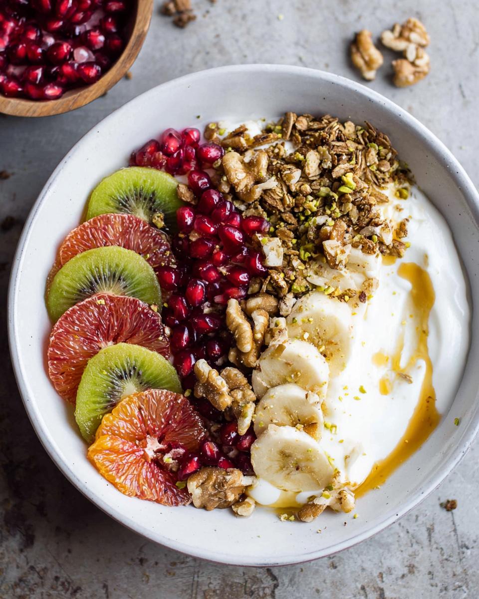 A vibrant and healthy Easy Yogurt Granola Bowl topped with kiwi, blood orange, pomegranate seeds, banana, walnuts, and granola.