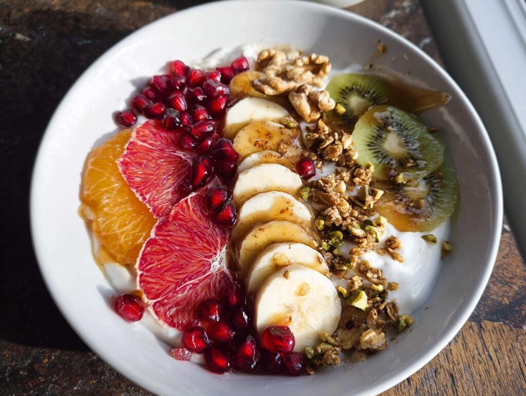 A vibrant and colorful Easy Yogurt Granola Bowl topped with banana, orange, blood orange, pomegranate, kiwi, and granola.