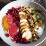 A vibrant and colorful Easy Yogurt Granola Bowl topped with banana, orange, blood orange, pomegranate, kiwi, and granola.