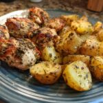 A plate of golden brown roasted chicken breast pieces and seasoned potatoes, seasoned with herbs.
