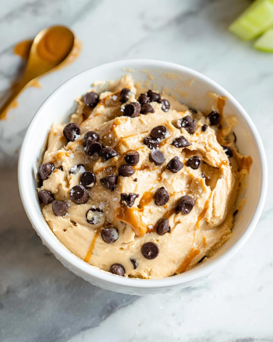 A bowl of delicious Greek Yogurt Cookie Dough topped with chocolate chips and a caramel drizzle.