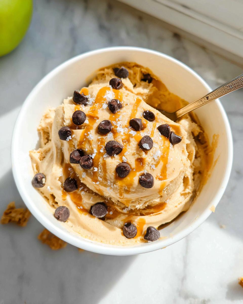 A bowl of creamy Greek yogurt cookie dough ice cream topped with chocolate chips, caramel drizzle, and sea salt.