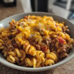 A bowl of cheesy taco pasta with ground beef and rotini pasta, topped with melted cheddar cheese.