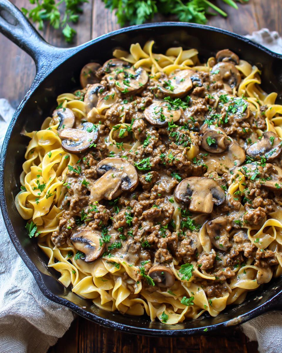 Close-up of a creamy beef stroganoff skillet meal with ground beef, mushrooms, and egg noodles, garnished with parsley.