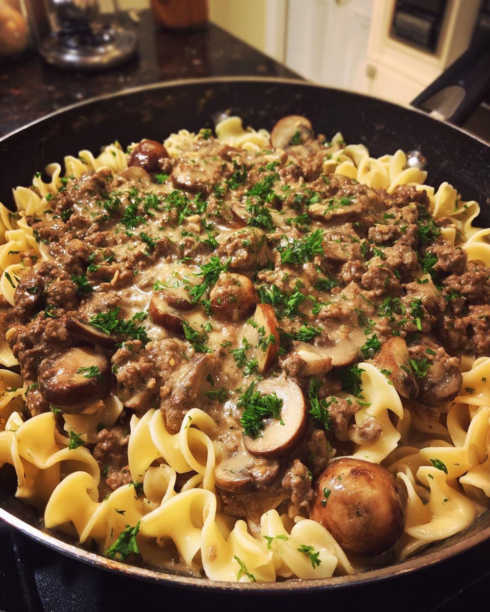 A close-up of a creamy ground beef stroganoff skillet meal with egg noodles and mushrooms, garnished with parsley.