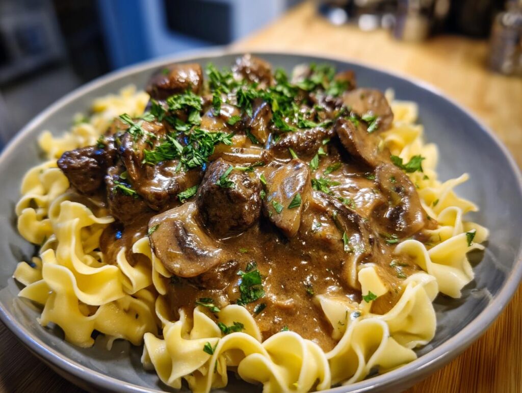 A close-up of a creamy beef stroganoff skillet meal served over egg noodles and garnished with fresh parsley.
