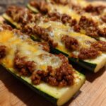 Close-up of baked zucchini boats filled with seasoned ground beef and topped with melted cheese.