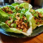 Close-up of fresh chicken lettuce wraps filled with seasoned ground chicken, topped with chopped peanuts and green onions.