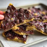 A hand holding a piece of Healthy Cookie Dough Bark, topped with chocolate chips and colorful sprinkles.