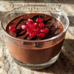 A close-up of a glass of High Protein Chocolate Pudding topped with pomegranate seeds and chocolate drizzle.