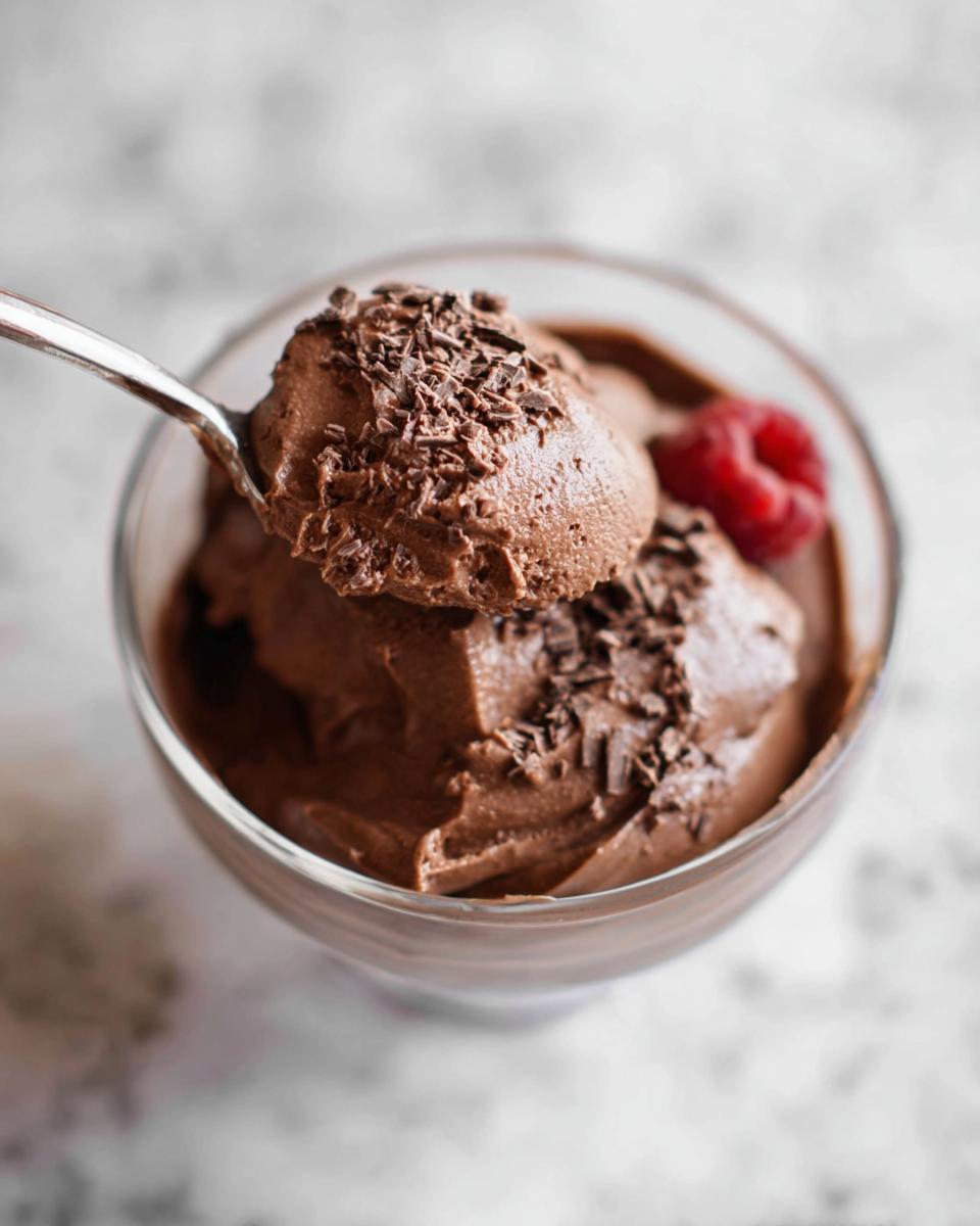 A spoonful of rich High Protein Chocolate Pudding topped with chocolate shavings and a fresh raspberry.
