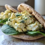 Close-up of a healthy lunch idea: high protein egg salad stuffed into a pita with fresh spinach.