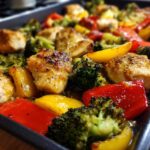 Close-up of honey mustard chicken breast pieces with broccoli and bell peppers on a sheet pan.