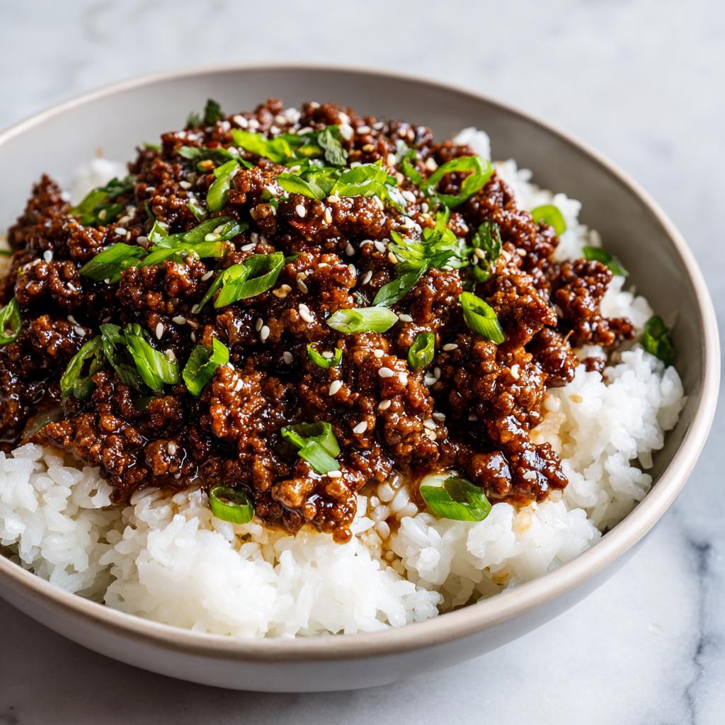 A close-up of a Korean beef rice bowl, featuring seasoned ground beef over white rice, topped with sesame seeds and green onions.