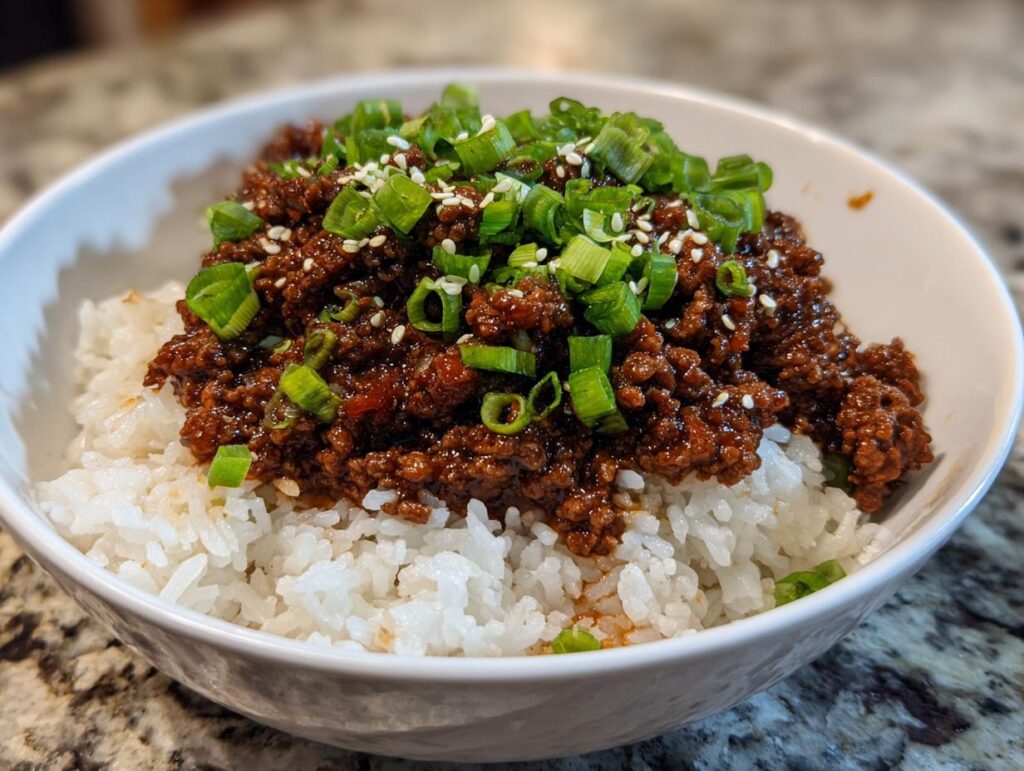 A close-up of a Korean beef rice bowl featuring seasoned ground beef over white rice, topped with chopped green onions and sesame seeds.
