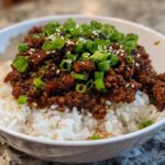 A close-up of a Korean beef rice bowl featuring seasoned ground beef over white rice, topped with chopped green onions and sesame seeds.
