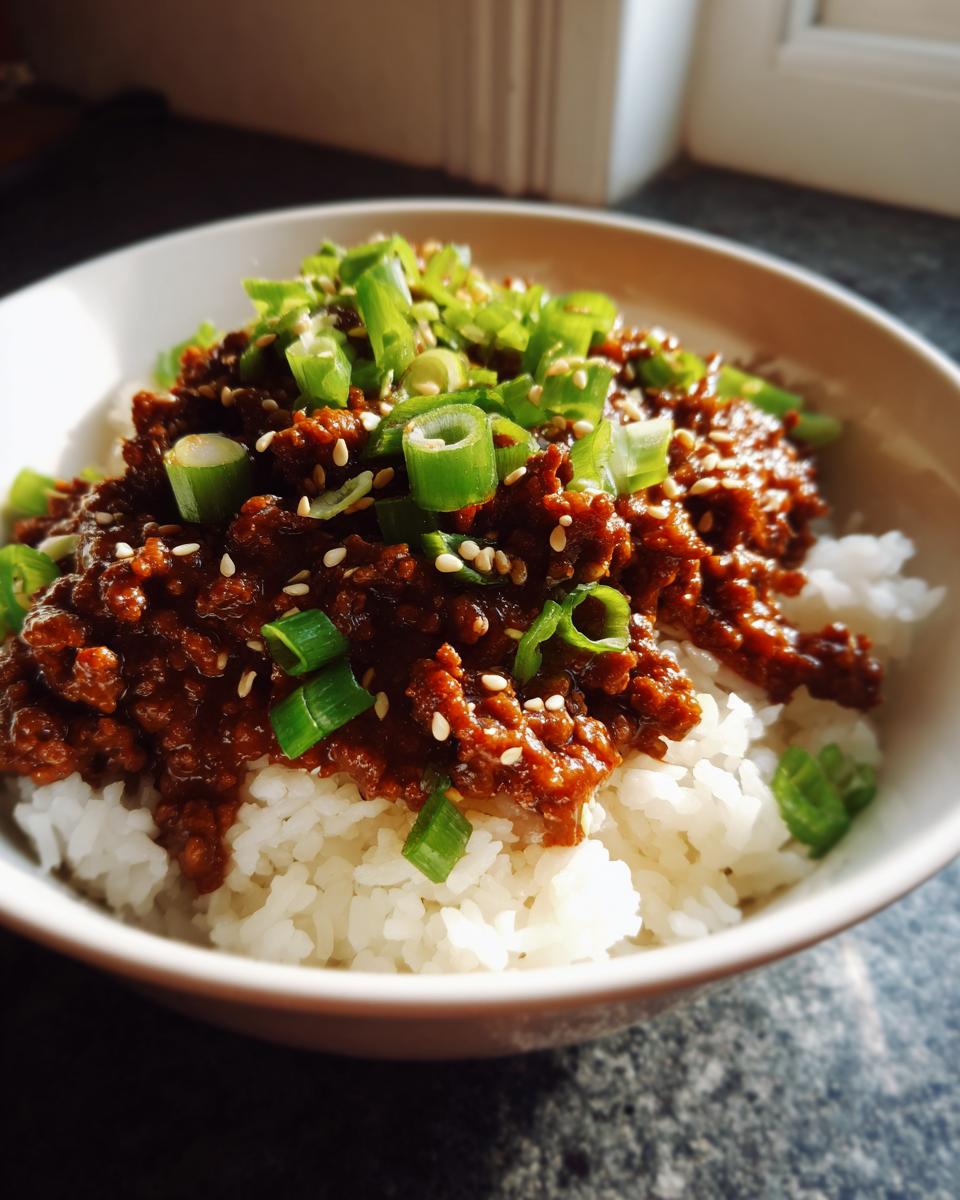 A close-up of a Korean beef rice bowl, featuring seasoned ground beef over white rice, topped with green onions and sesame seeds.