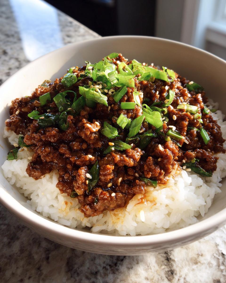 A close-up of a Korean beef rice bowl, featuring seasoned ground beef over white rice, topped with green onions and sesame seeds.