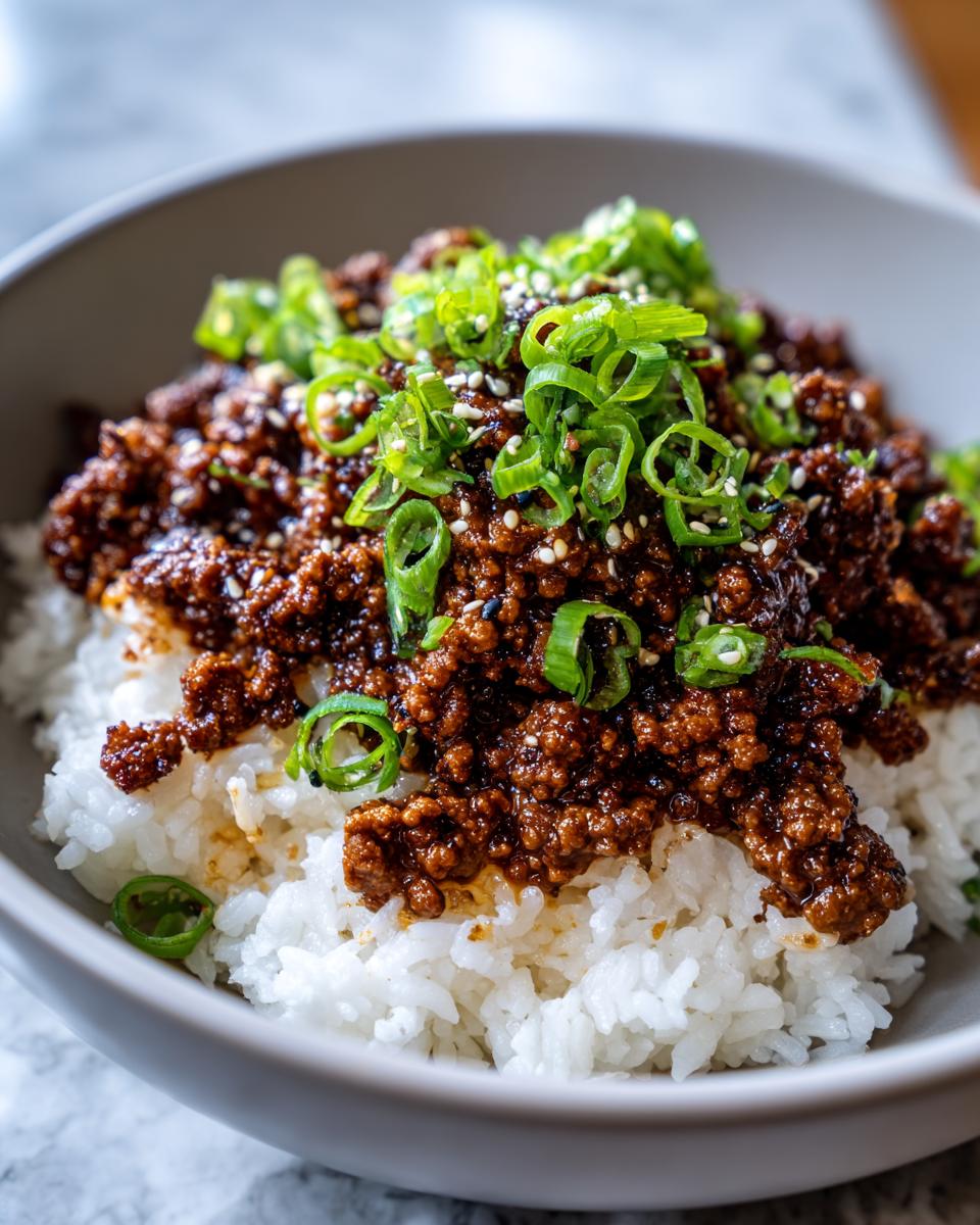 A close-up of a Korean beef rice bowl featuring seasoned ground beef over white rice, topped with green onions and sesame seeds.