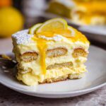 A decadent slice of Lemon Tiramisu, layered with ladyfingers and creamy lemon filling, topped with lemon slices and powdered sugar.