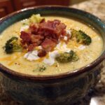 A hearty bowl of loaded broccoli cheddar soup topped with crispy bacon, shredded cheddar cheese, and a dollop of sour cream.