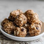 A white bowl filled with delicious no-bake chocolate peanut butter protein balls, showing oats and chocolate chips.