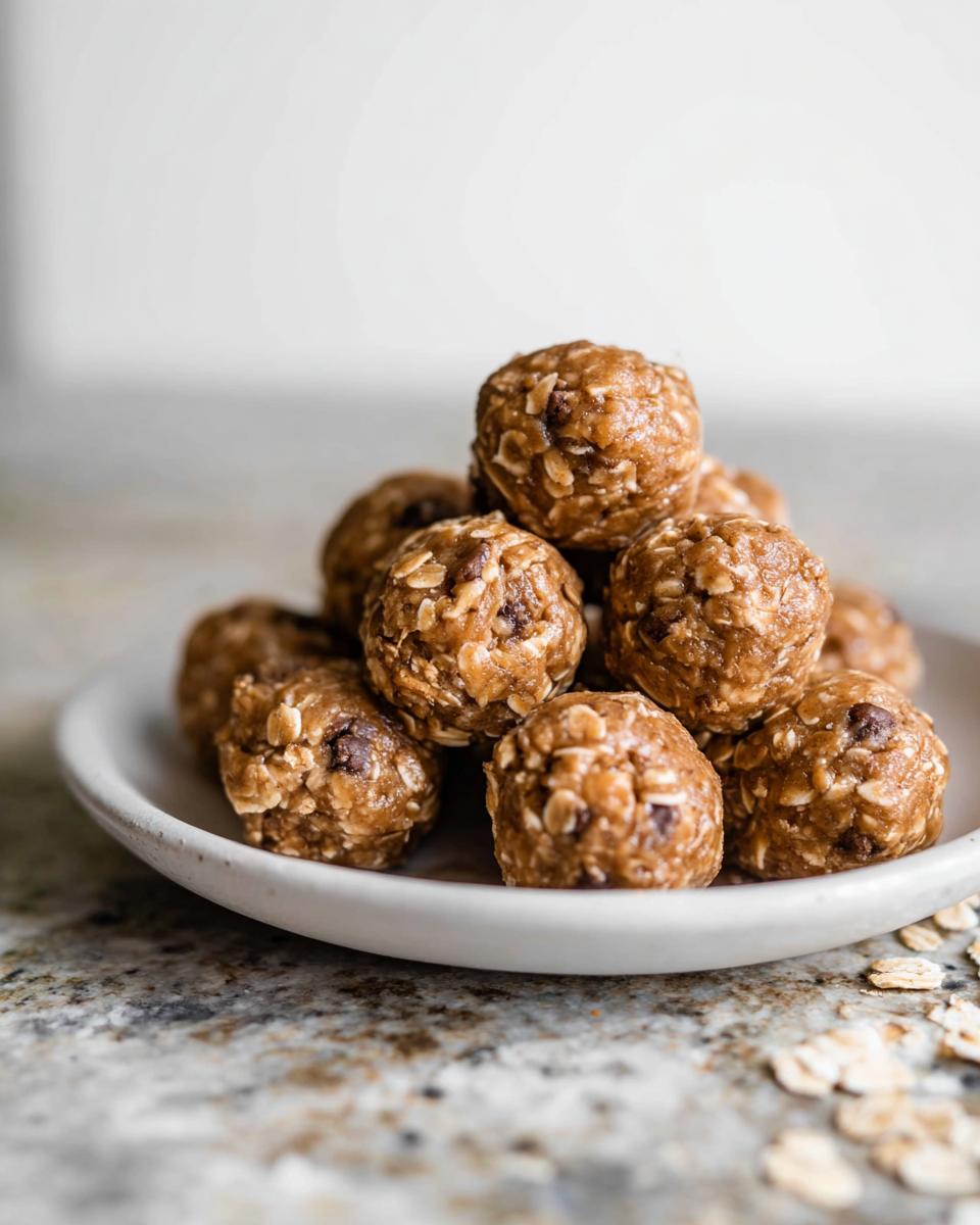 A pile of no-bake chocolate peanut butter protein balls with oats and chocolate chips on a white plate.