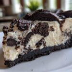 A slice of no bake Oreo cheesecake on a white plate, featuring a chocolate cookie crust and creamy filling with Oreo crumbles.