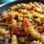 Close-up of a one pot taco pasta dish with rotini noodles, seasoned ground beef, diced tomatoes, and melted cheddar cheese.