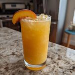 A refreshing glass of peach recipes with iced tea slush, garnished with a peach slice.