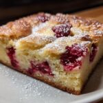 A slice of raspberry white chocolate blondies, dusted with powdered sugar, on a white plate.