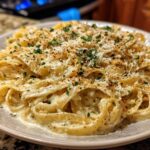 A close-up of fettuccine pasta coated in a rich, creamy Alfredo sauce, topped with grated Parmesan and parsley.