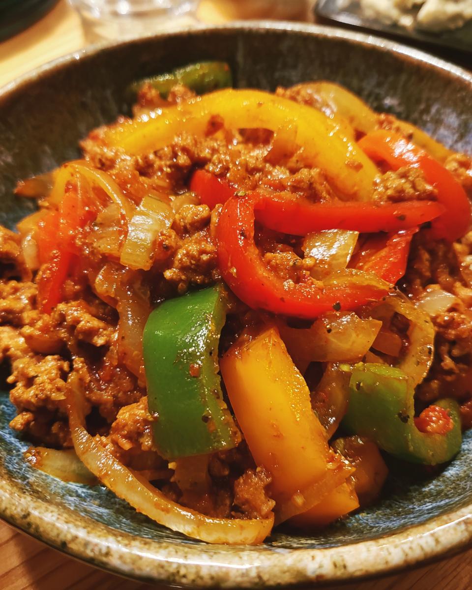 Close-up of a bowl filled with sausage, peppers, and onions, a delicious comfort food dish.