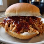 A delicious pulled BBQ chicken sandwich made with slow cooker recipes, piled high on a bun with BBQ sauce.