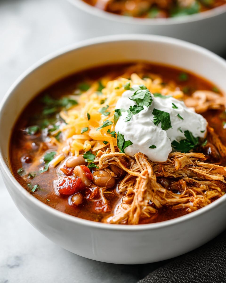 A bowl of flavorful slow cooker white chicken chili topped with shredded cheese, sour cream, and cilantro.