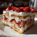 A slice of creamy strawberry icebox cake layered with cookies, whipped cream, and fresh strawberries.