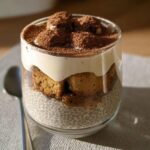 A layered Tiramisu Chia Pudding in a glass, topped with cocoa powder and ladyfingers.