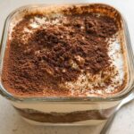 A close-up of Tiramisu Chia Pudding with Greek Yogurt, topped with cocoa powder, in a glass dish.