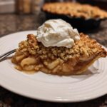 A slice of warm and buttery apple crisp topped with a scoop of melting ice cream on a white plate.