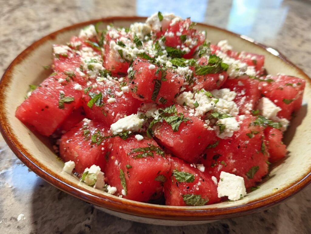 Close-up of a refreshing summer salad with cubed watermelon, crumbled feta cheese, and fresh mint leaves.