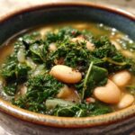 A close-up of a bowl of white bean kale soup, showcasing tender white beans and vibrant kale in a savory broth.